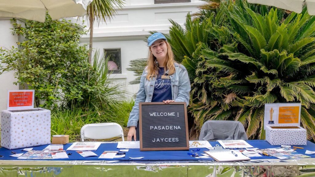 Pasadena Jaycees president standing with "Welcome Pasadena Jaycees" sign